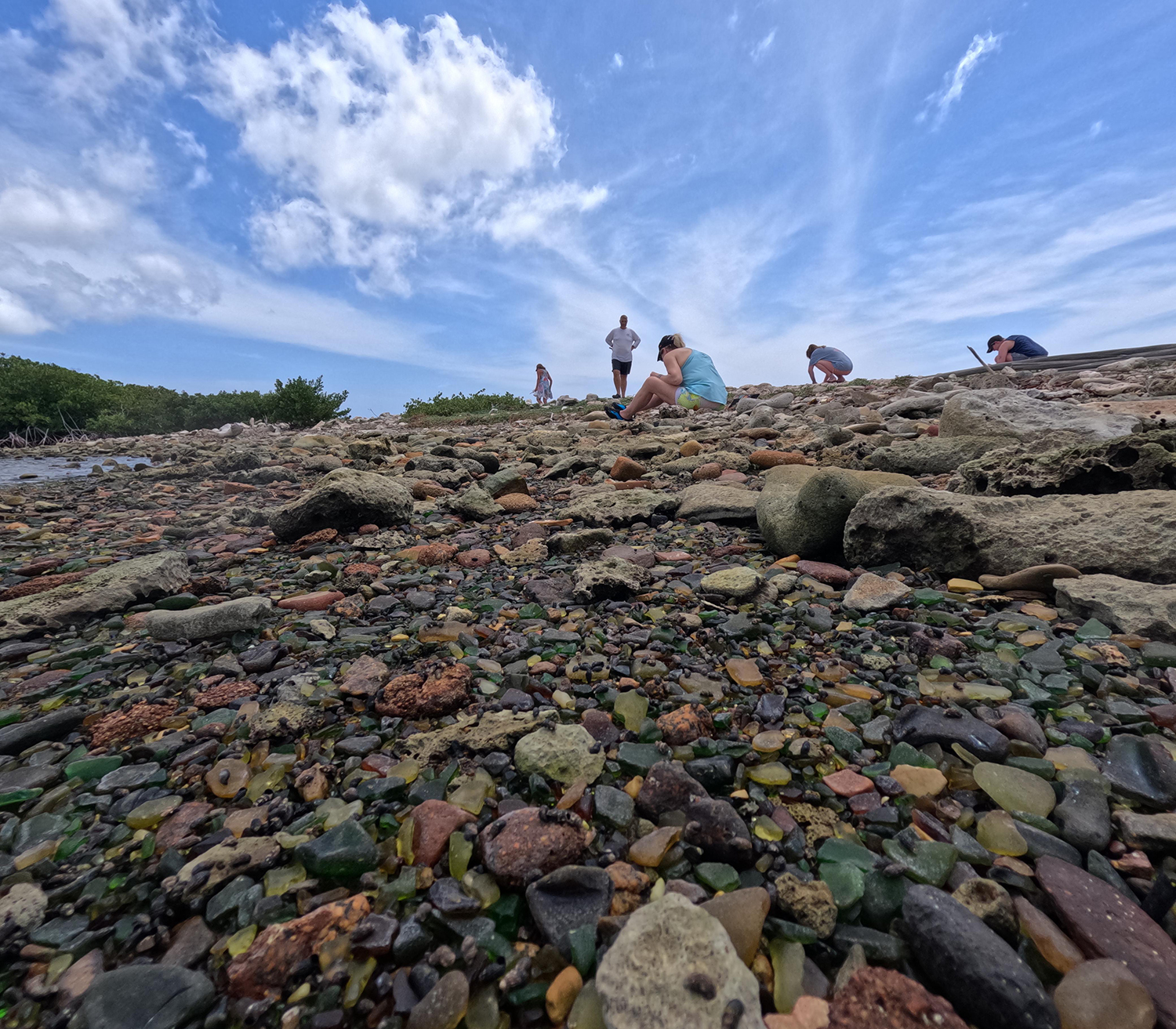 Tour participants search for sea glass along the rocky shore of Sea Glass Island Aruba.