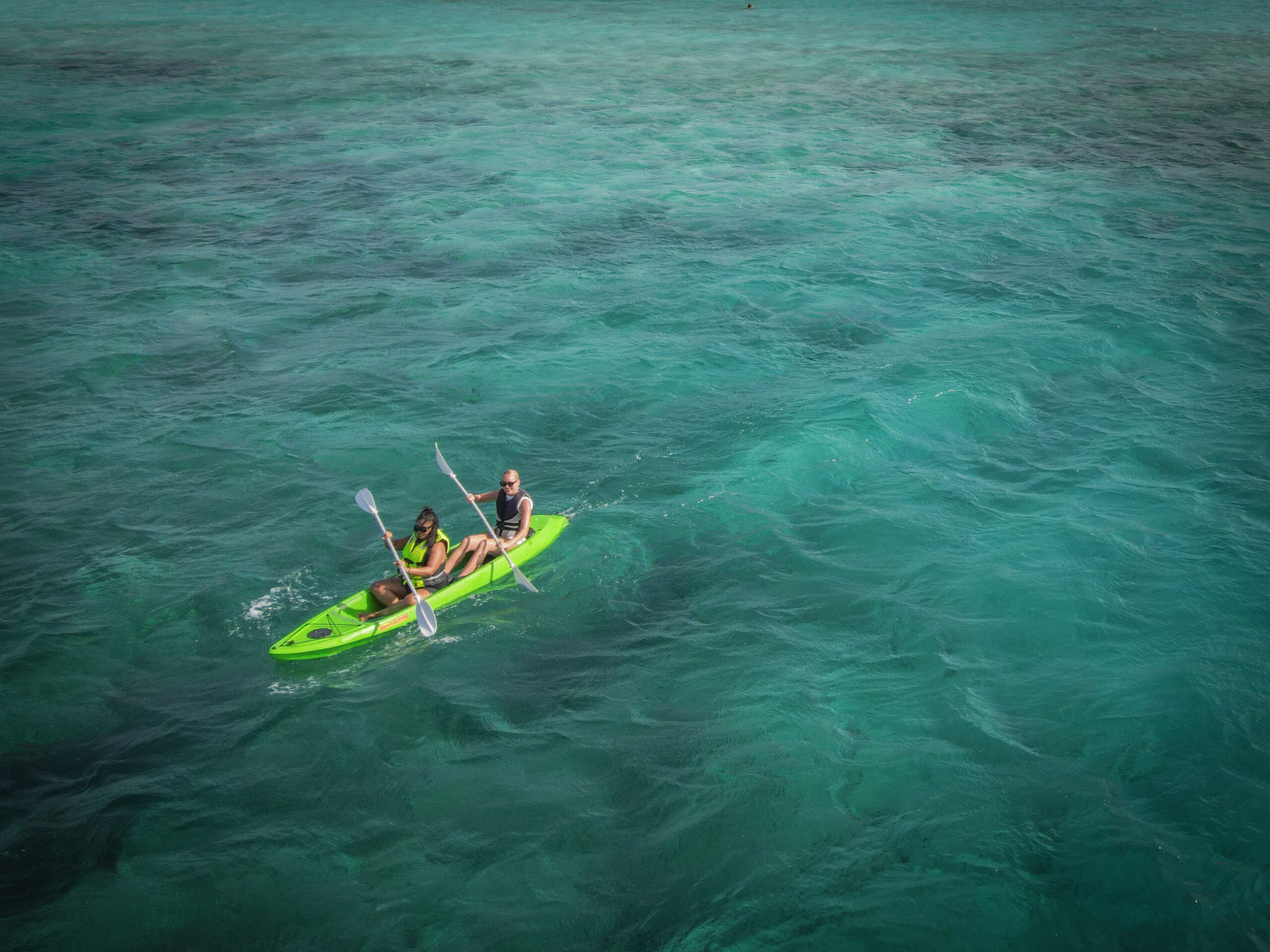 Two women paddling a green tandem kayak over rich turquoise seas off the coast of Aruba.