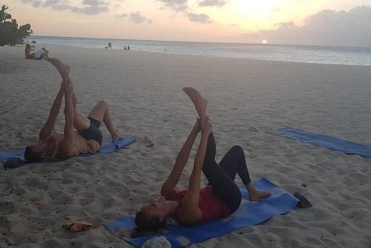Two people lying on their backs on yoga mats, stretching their hamstrings, a gentle and restorative pose suitable for all levels welcome to sunset Beach Yoga.