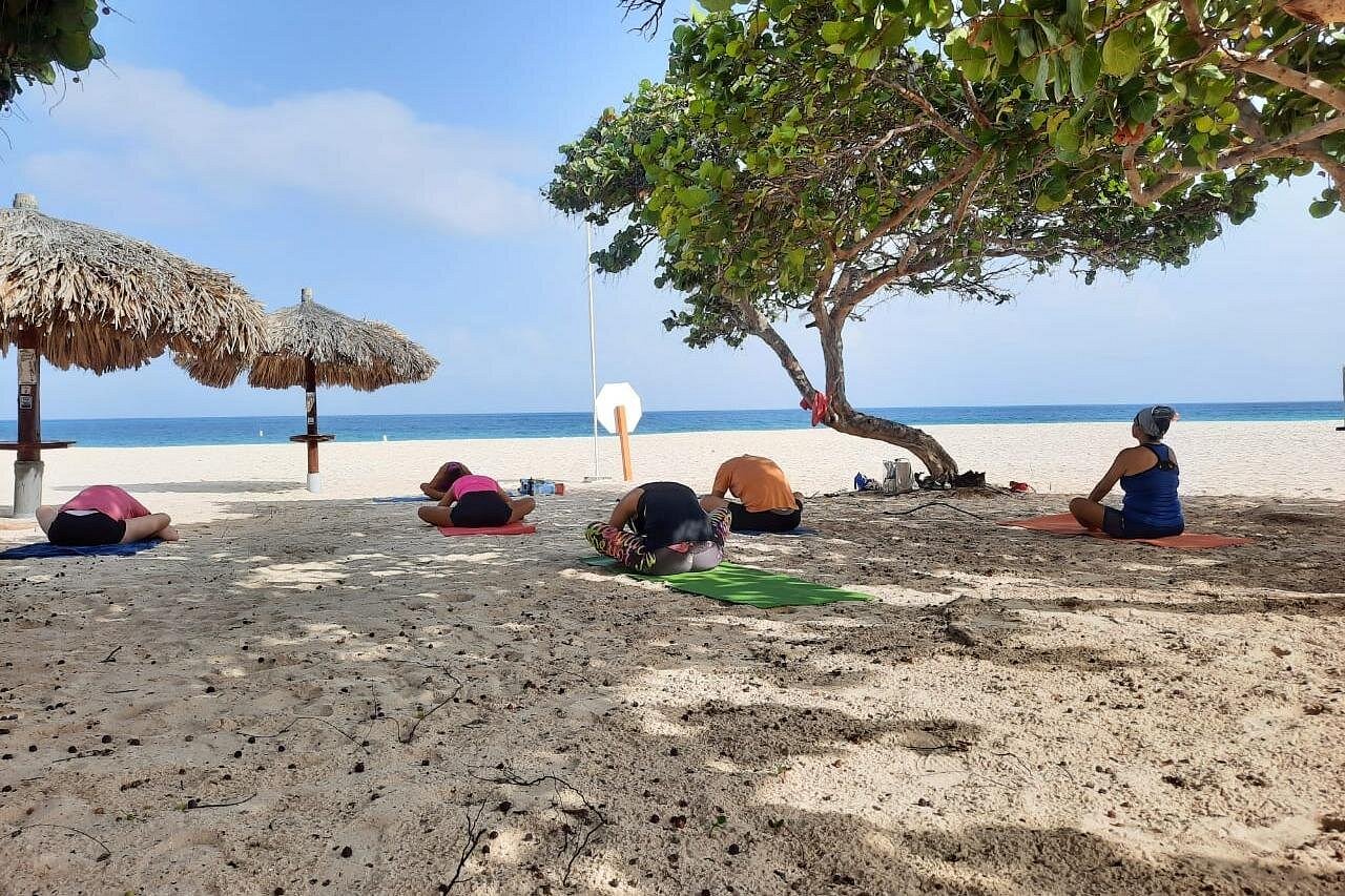A group relaxing in Child's Pose (Balasana) under the shade, a restorative posture suitable for all levels welcome, perfect after Beach Yoga or during a meditation session.