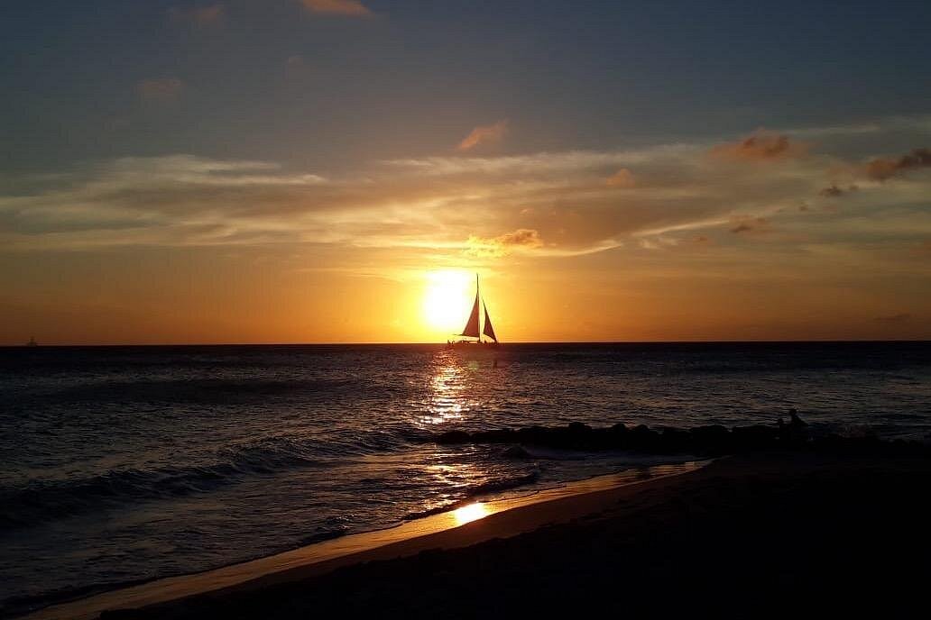 A picturesque view of a sailboat silhouetted against a brilliant orange sunset over the ocean, symbolizing tranquility and the perfect ambiance for Sound Bath & meditation.