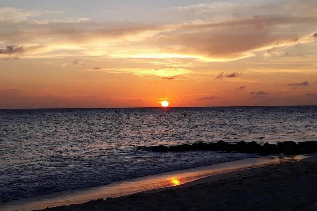 A serene photo of a vibrant orange sunset over the dark ocean, ideal for a tranquil Sound Bath & meditation session on the beach.